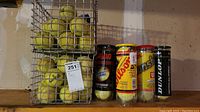 Photo showing two wire baskets filled with used tennis balls and four tubes of tennis balls from brands Penn, Wilson, USTA, and Dunlop