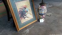 Framed print and Asian themed lamp seen together on concrete floor, showing both items' general size and style.