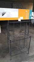 Black metal stand with decorative scroll designs, two lower shelves, and space above for the pop-up closet