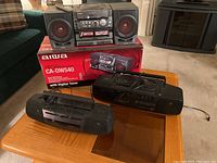 Aiwa CA-DW540 boombox with box shown on table, including two black and red speakers and cassette/CD player unit with control buttons.