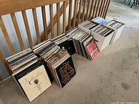 Four record crates and loose boxes of LPs lined up along banister on floor.