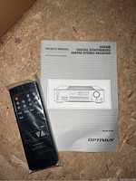 Image of Optimus owner's manual and remote control in plastic wrapping, placed on wooden surface.