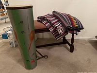 Bongo drum next to piano bench with two folded blankets on the bench, showing overall lot contents.