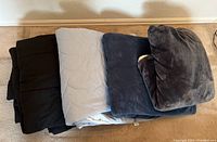 Lot of 4 folded comforters in different colors on floor against wall