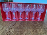 Six stemmed Cristal d'Arques Longchamp glasses neatly arranged inside the original red interior packaging, showing crystal pattern and faceted stems.