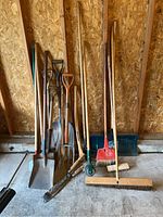 Full view of the lot showing all gardening tools grouped against plywood wall in garage