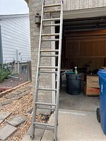 Aluminum extension ladder leaned against garage, visible rungs and side rails.