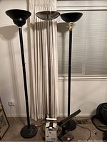 Three black metal floor lamps with upward-facing bowl-shaped shades and one with brass accent, standing upright in a room.