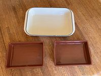 Top view of white LeCreuset baking dish and two smaller brown Sur La Table ceramic baking dishes arranged on wooden surface.