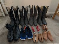 Front and side view of four pairs of cowboy boots, one pair of black shoes, and six shoe stretchers arranged on floor.