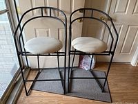 Two matching bar chairs with black metal frame and white round seats viewed front and side.