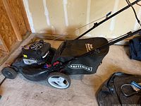 Side view of black Craftsman self-propelled lawnmower with Grass Blocker bag, showing metal deck, wheels, and engine area.