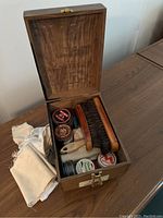 Open wooden box showing the contents including shoe polish tins, brushes, and cloths
