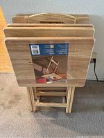 Five wooden TV trays standing folded together, one featuring original label on top.