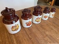 Five vintage McRoy Pottery Fruit Festival canisters arranged in descending size, each showing fruit patterns and brown lids.