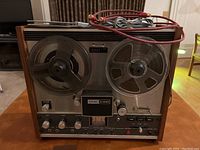 Front view of the TEAC A-1230 tape deck showing reels, control knobs, VU meter, and wood side panels.