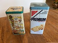 Two vintage decorative food storage tins: Uncle Ben's Rice and Nabisco Premium Saltine Crackers. Both metal with vibrant vintage graphics.