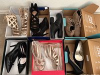 Top view photo showing six pairs of women's shoes in their original boxes, including high heels, boots, and sandals in nude, black and taupe colors.