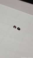 Two loose oval shaped sapphires placed on a white surface, showing their color and cut.