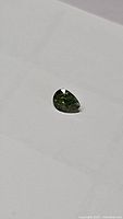 Close up photo of a pear cut green sapphire on white background showing the facets and color.