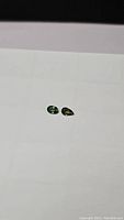 Photo showing two small faceted green sapphires: one oval-shaped and one pear-shaped, both on white background
