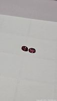Two small oval purple-pink tourmaline gemstones placed on a white surface, showing shape, size and color.