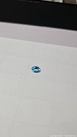 Oval cut natural Swiss blue topaz gemstone on a plain light background showing bright lagoon blue color and facet details