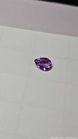 Pear cut purple amethyst gemstone laying on a light surface, showing its shape and color
