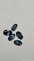 Five natural calibrated oval cabochon blue sapphires lying on a neutral surface, showing their deep blue color and polished cabochon cut.