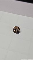 Round brown smokey quartz gemstone with diamond cut facets, showing reflections and clarity under light on white background.