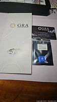 GRA certification booklet with the moissanite gemstone and warranty card in sealed packaging showing the stone and certification number.