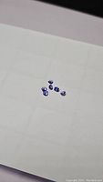Six deep purple-blue pear cut tanzanite gemstones arranged on a white sheet, showing overall size and color.