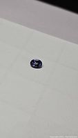 Oval cut natural tanzanite gemstone shown on white surface highlighting deep blue-purple internal coloration and clarity.