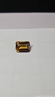 Emerald cut deep golden citrine gemstone placed on white background, showing rectangular shape and stepped facets.