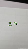 Four loose marquis cut gemstones placed on a white surface exhibiting deep green color from chromium content, with glossy facets visible.