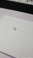 Oval teal green aquamarine cabochon gemstone on a white grid background, showing the smooth domed top and rounded edges.