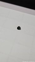 Close-up image of a small green teardrop-shaped sapphire gemstone on white background.