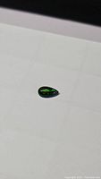 Pear-shaped cabochon black opal showing rich green patches on a dark body tone under bright light.