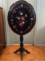 Full view of the antique papier mache table in upright tilt position showing floral design and ornate scalloped edges.