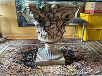 Close-up image of the garden cement urn base showing detailed acanthus leaf carvings and cupid sculptures on each side, square base pedestal.