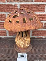 Front view of rusty cast metal mushroom garden light with perforated cap and textured stem and base.