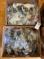 Two banana boxes filled with bags of assorted costume jewelry pieces including necklaces, bracelets, earrings, brooches, and rings.