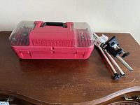 Full view of Craftsman red carrying case with clear lids showing assorted rotary tool bits inside, and metal tool stand with clamp beside it on wooden surface.