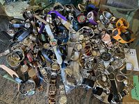 Photo showing a large variety of men's and ladies' wristwatches in assorted styles, placed on a glass surface. Includes analog, digital, sport and dress watches made of metal, leather, plastic, and fabric.