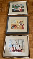 Three framed John Lim prints stacked vertically on a parquet floor, showing colorful Asian scenes with figures in traditional clothing.
