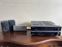 Photo showing Pioneer stereo receiver and three Realistic speakers (two black satellites, one white center channel) on wooden surface against wall.
