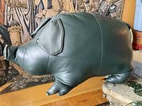 Side profile of green leather pig ottoman showing overall shape and legs