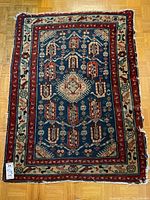 Full view of the small Persian carpet showing overall design and condition on wood floor.