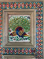 Full view of the vintage enameled peacock tin panel with colorful decorative frame.