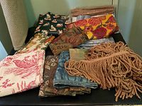 Full view of various vintage fabrics and twisted fringe trim pieces laid out on a black surface showing color and texture variety